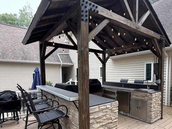 Outdoor kitchen with stone bar, built-in grill, and gable roof structure