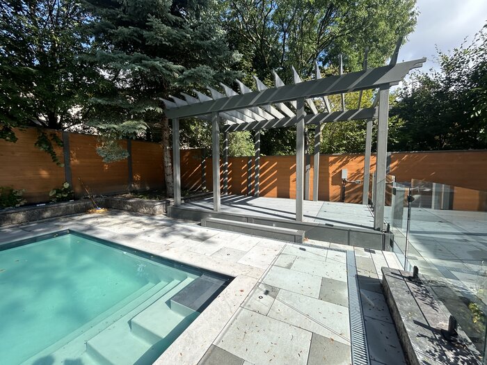 Grey post-and-beam pergola over a composite deck beside a pool